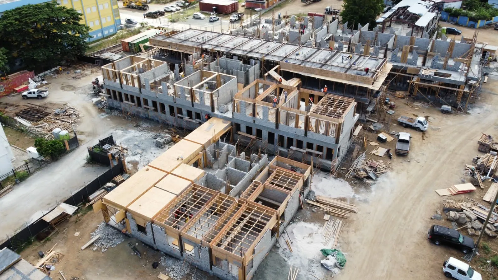 Aerial view of a large building under construction showing concrete walls, wooden framing, construction materials, and workers on site.