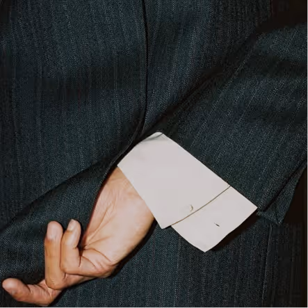 Close-up of a hand tucked into the sleeve of a dark pinstripe suit jacket, with a white shirt cuff visible.