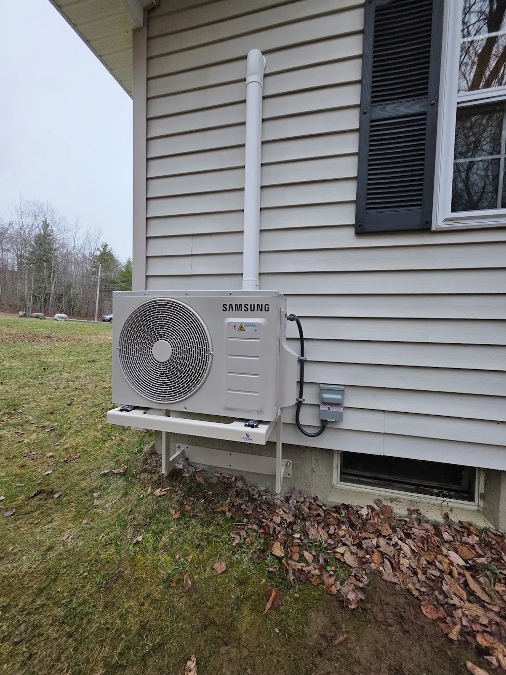 Samsung outdoor heat pump unit mounted on a beige house wall with a grassy yard.