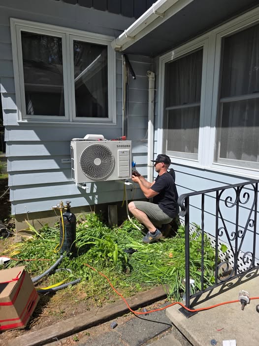 Technician installs or repairs a Samsung heat pump unit mounted on a house exterior wall.