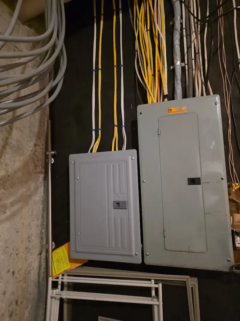 Two electrical breaker panels mounted on a wall with neatly organized yellow and white cables.