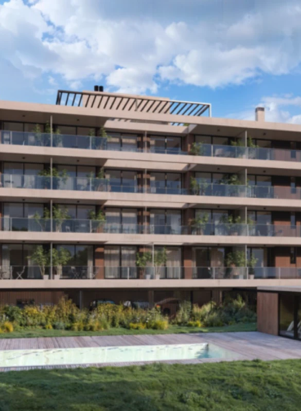 Modern multi-story building with glass balconies overlooking a lawn and small pool under a blue sky.