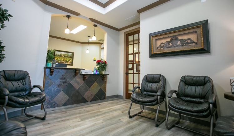 Comfortable dental office waiting room with black leather chairs, modern flooring, decorative artwork, warm lighting, and a welcoming front reception desk designed to create a relaxing patient experience