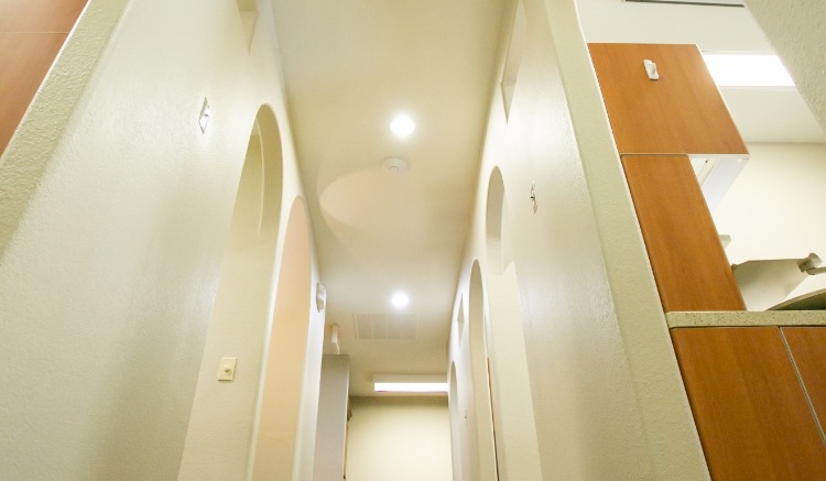 Bright hallway inside a modern dental office featuring arched doorways, recessed ceiling lighting, neutral-colored walls, and warm wood cabinetry that creates a clean and welcoming atmosphere