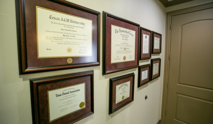 Framed dental degrees, certifications, and professional credentials displayed on the wall inside a dental office hallway, highlighting the experience and education of the dental team in a clean and professional environment