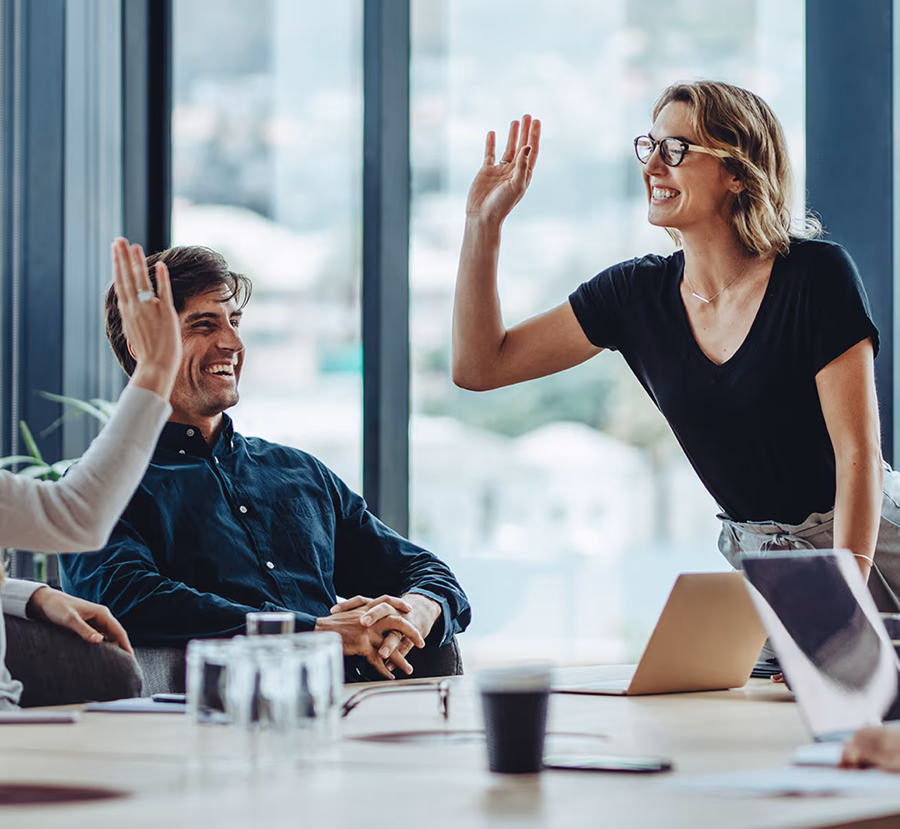Smiling woman in glasses giving a high-five to a seated man in a meeting room.