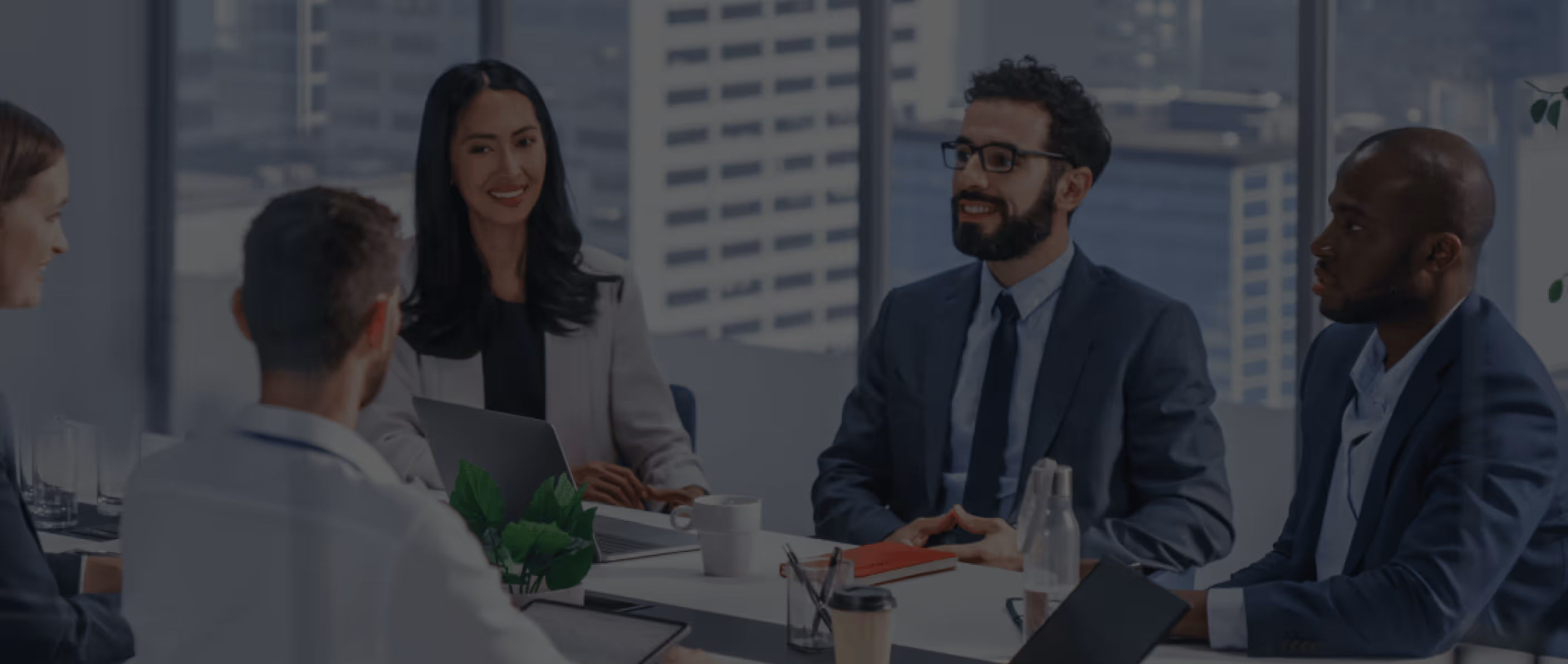 Five diverse business professionals in a meeting around a table with laptops and coffee cups.