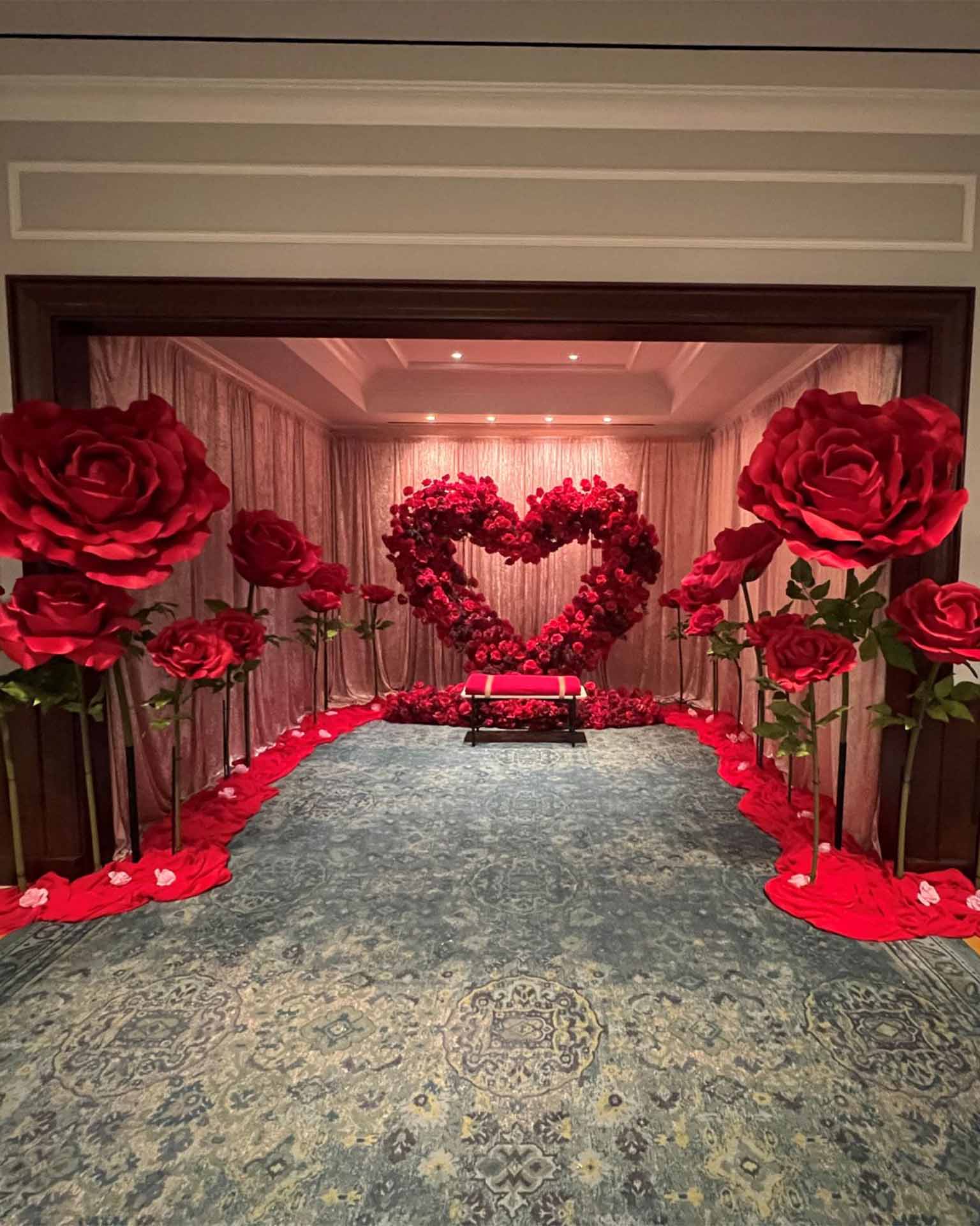 Room decorated with a red rose heart center, giant red roses, and a red bench on a blue patterned carpet.