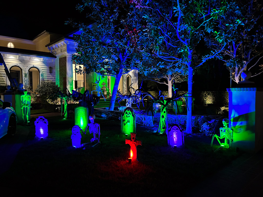 Front yard decorated with glowing skeletons and tombstones for Halloween at night.