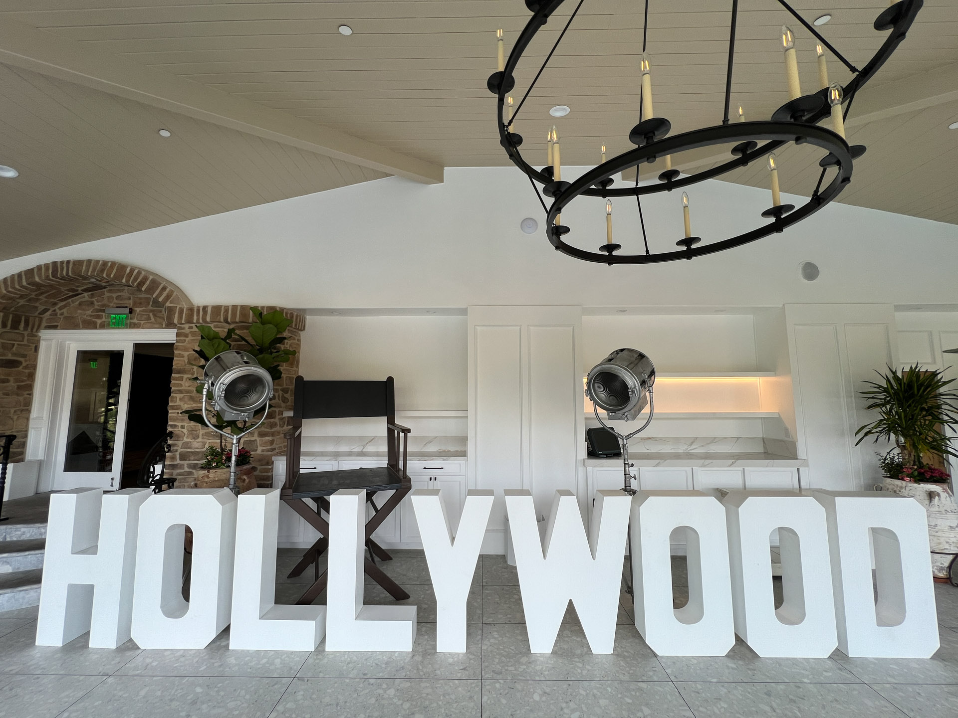 Large white letters spelling 'HOLLYWOOD' with two studio lights and a director's chair indoors.