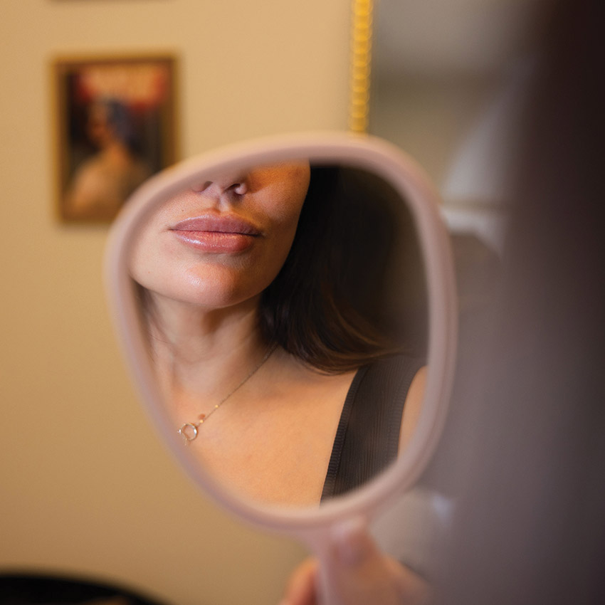 Patient viewing lips after lip filler treatment in a handheld mirror.