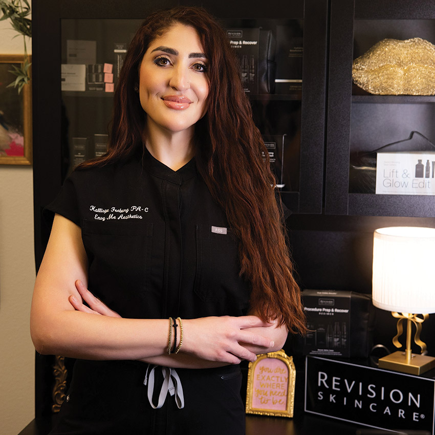 Kalli standing in front of a cabinet of medical-grade Revision Skincare products used in personalized skincare treatment plans.