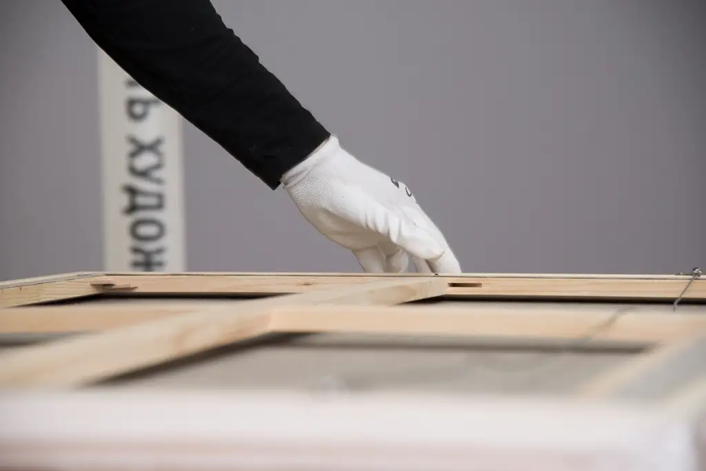 Victorins - gloved hand carefully adjusting a wooden frame during art restoration