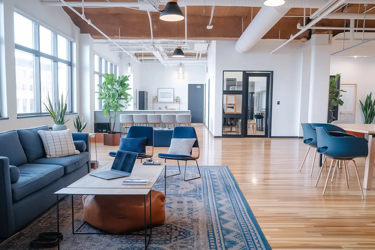 Modern office lounge with blue sofa, two blue chairs, coffee table, and large windows.