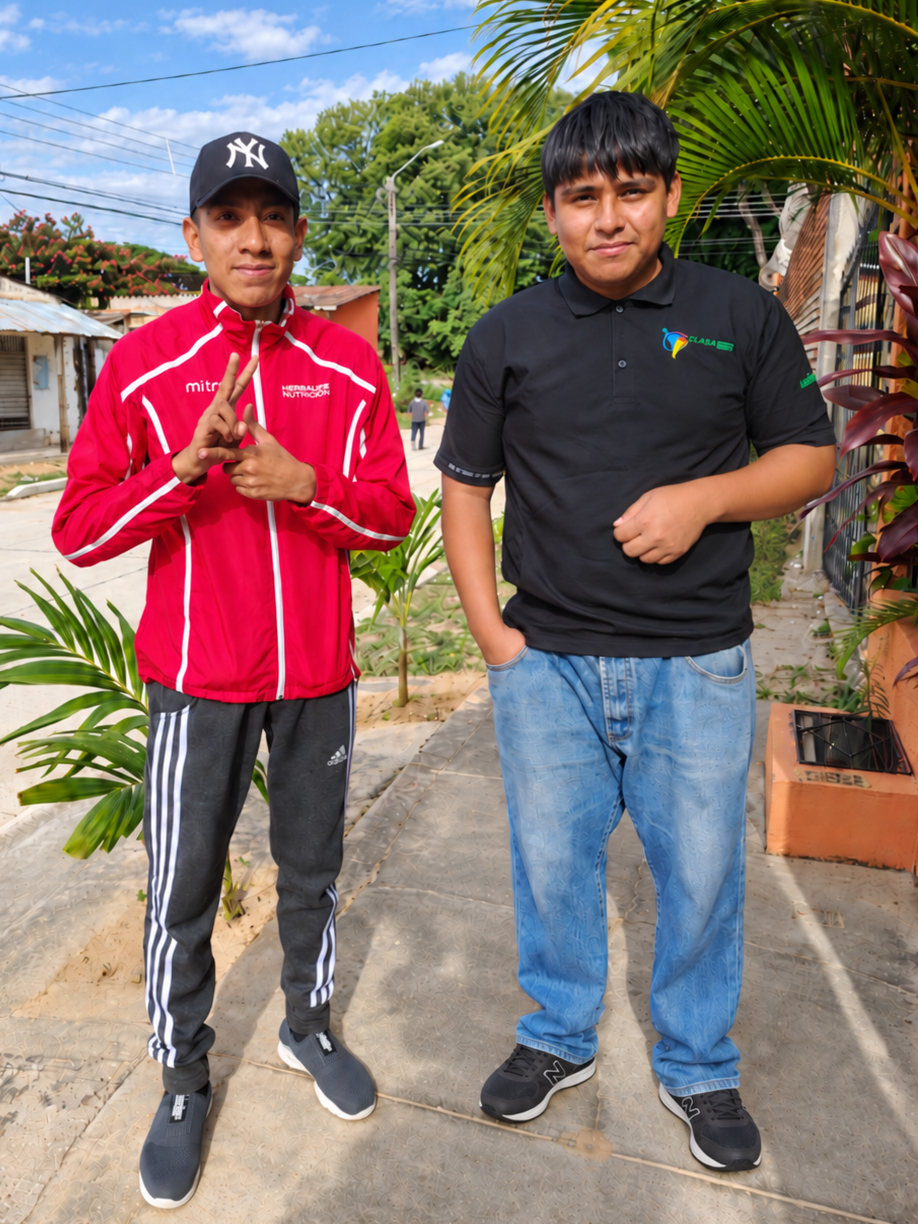 Two young adults standing outdoors beside plants.