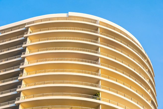 Curved modern apartment building balconies with yellow lighting against clear blue sky.