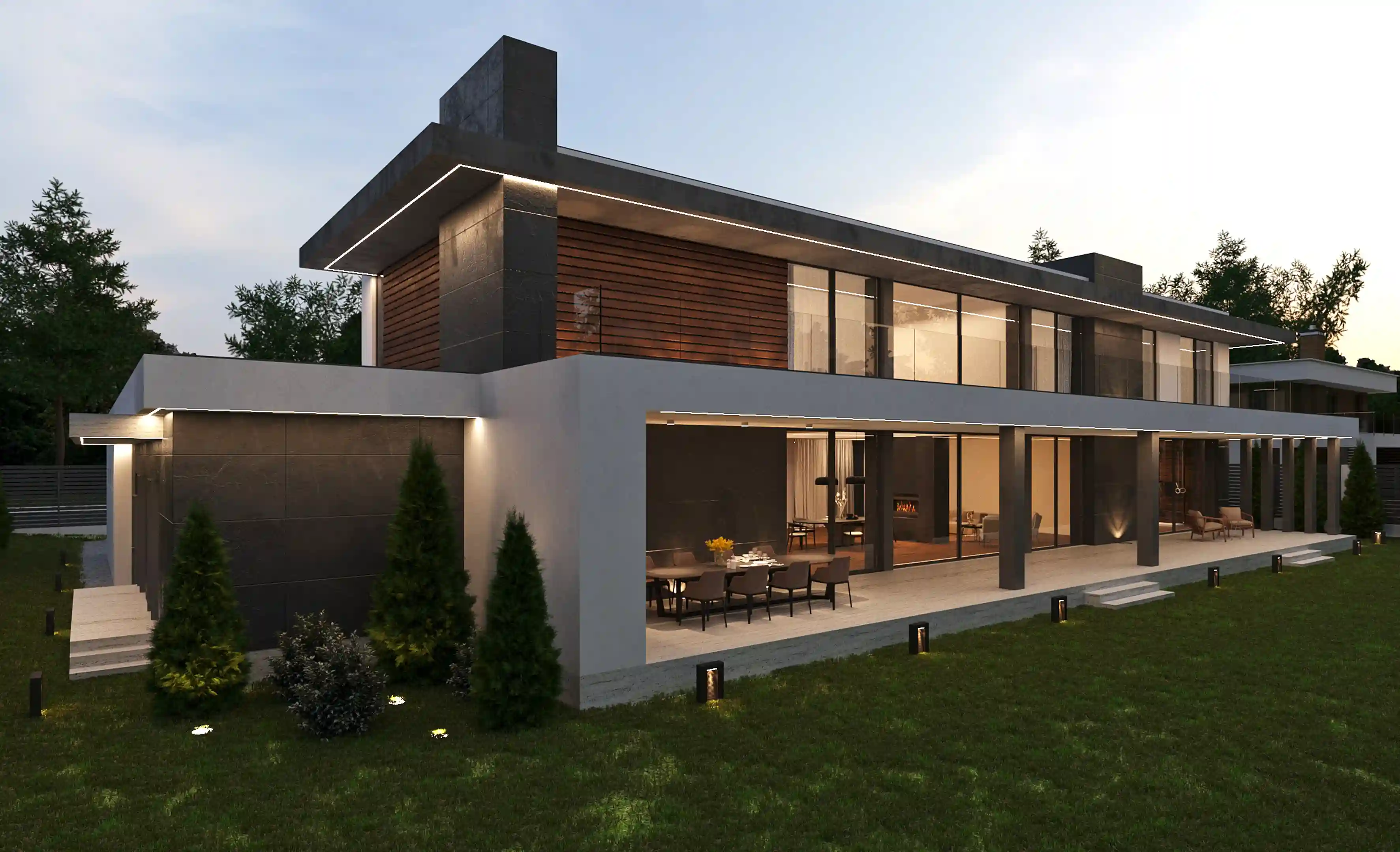 Modern two-story house with large glass windows, patio dining area, and outdoor lights on a lawn at dusk.