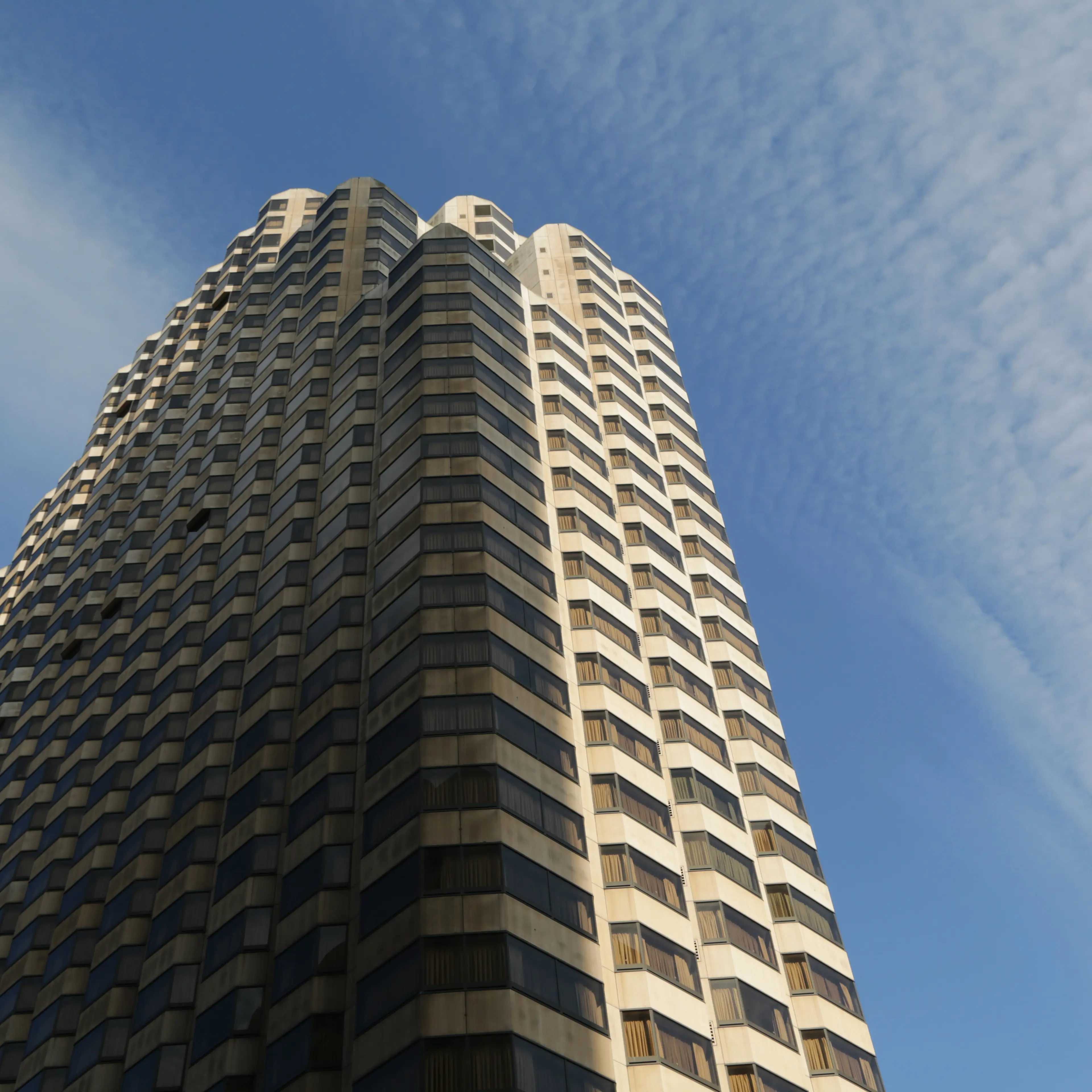 Low-angle view of a tall modern building with a pattern of windows against a blue sky with light clouds.