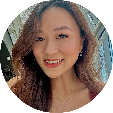 Smiling woman with long brown hair wearing earrings and makeup, with a windowed background.