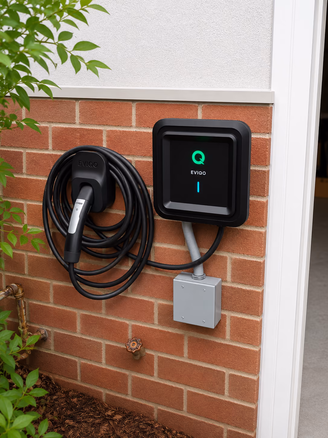 EVIQO electric vehicle charger mounted on brick wall with coiled charging cable and plug.