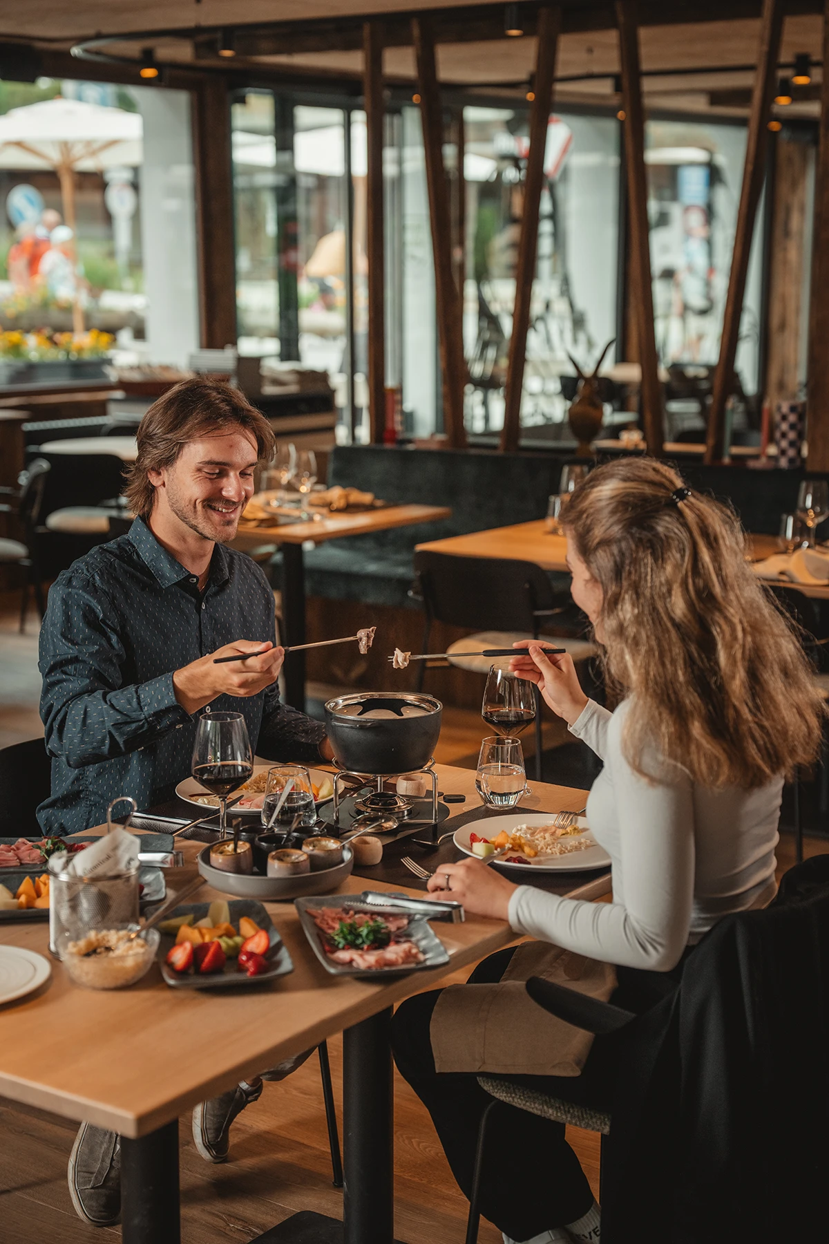 Paar geniesst Fondue mit Fleischplatte und Beilagen im Restaurant Ribis & Stibis in Täsch