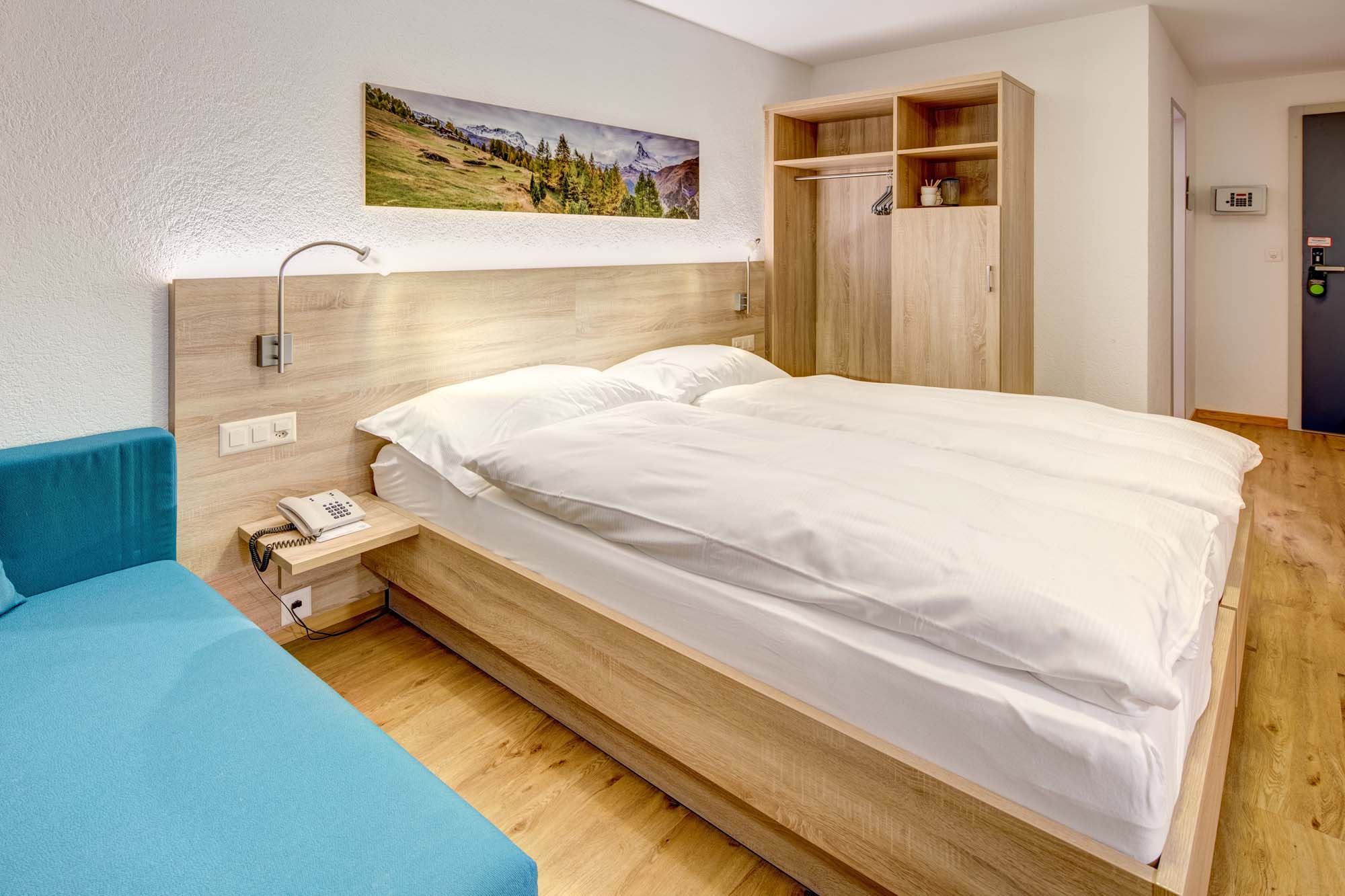 Superior Doppelzimmer mit Doppelbett, blauem Sofa, Bergpanorama-Bild und Einbauschrank im Matterhorn Inn in Täsch