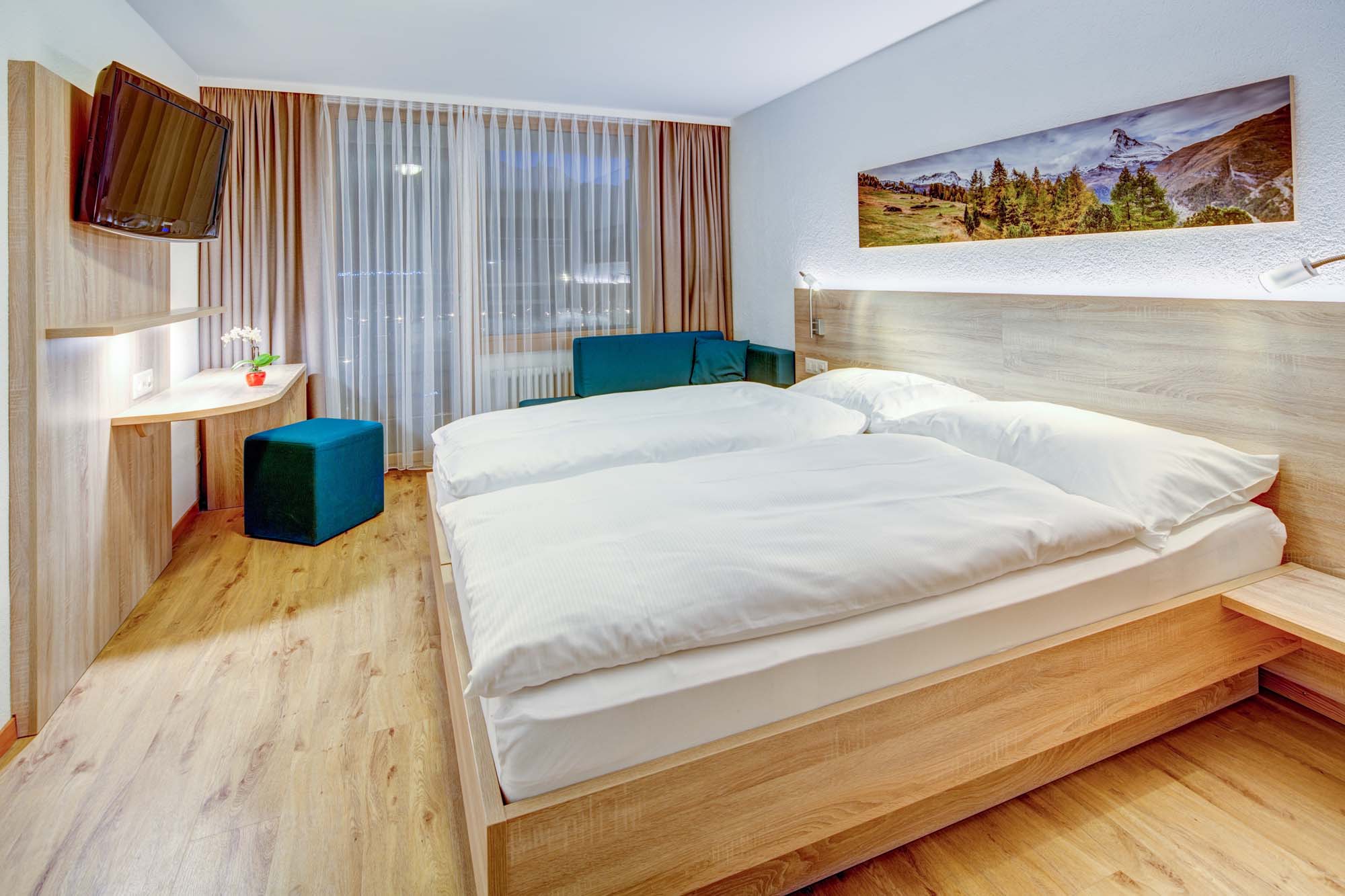 Superior Doppelzimmer mit Doppelbett, Schreibtisch, TV und Sitzecke am Fenster im Matterhorn Inn in Täsch