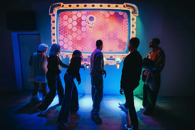 Audience watching a show featuring animated characters Ladybug and Cat Noir with green and red stage lights and the text 'Paris a besoin de toi'.