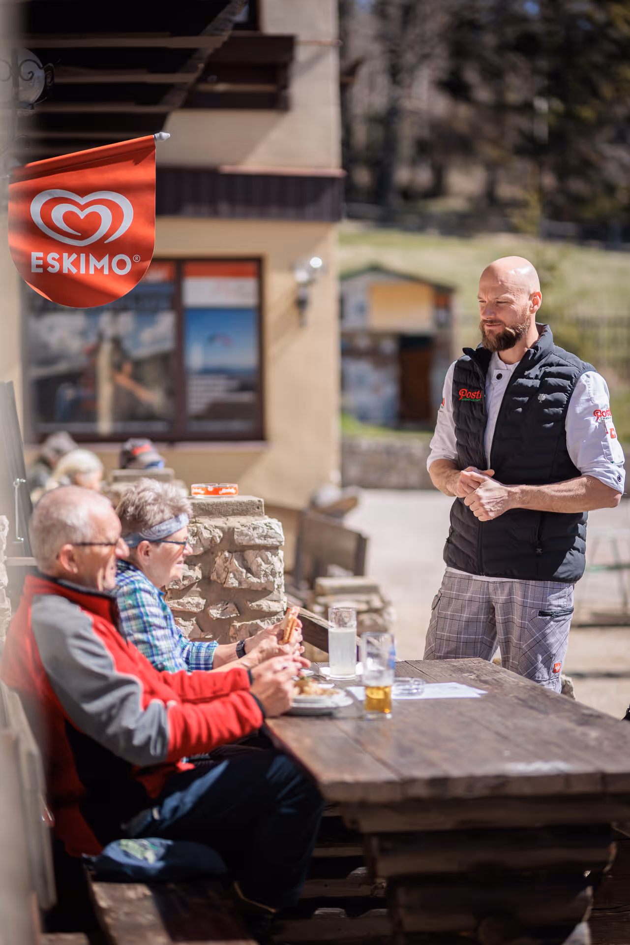 Gastgeber bedient Gäste im sonnigen Gastgarten des Alpengasthof Postl