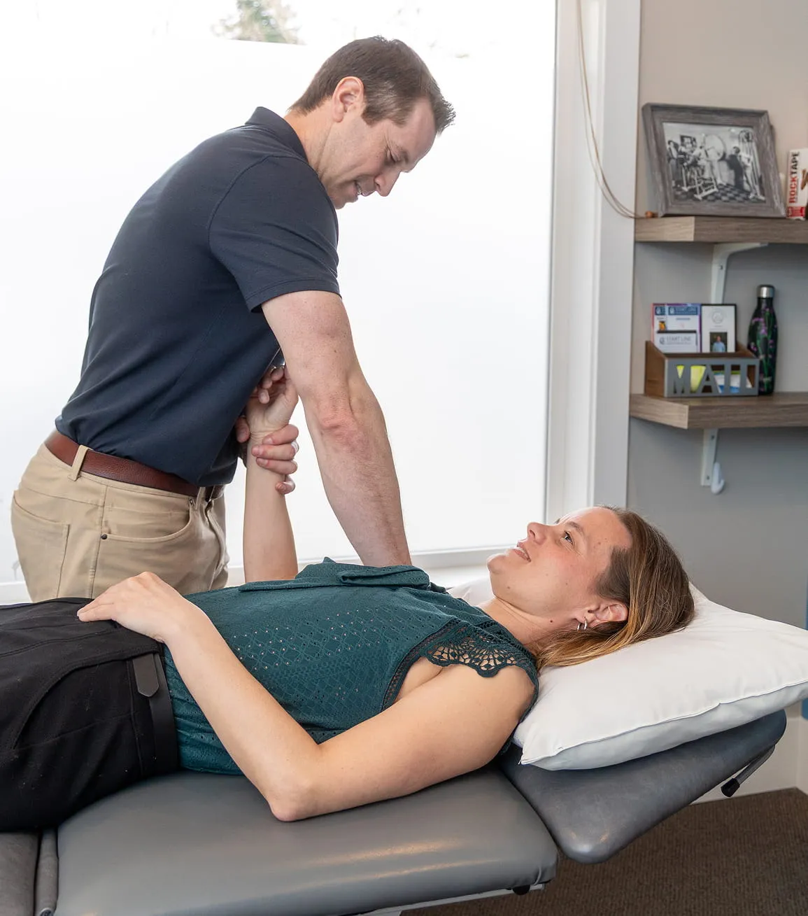 Physical therapist performing arm stretch on a woman lying on a treatment table with a pillow under her head.