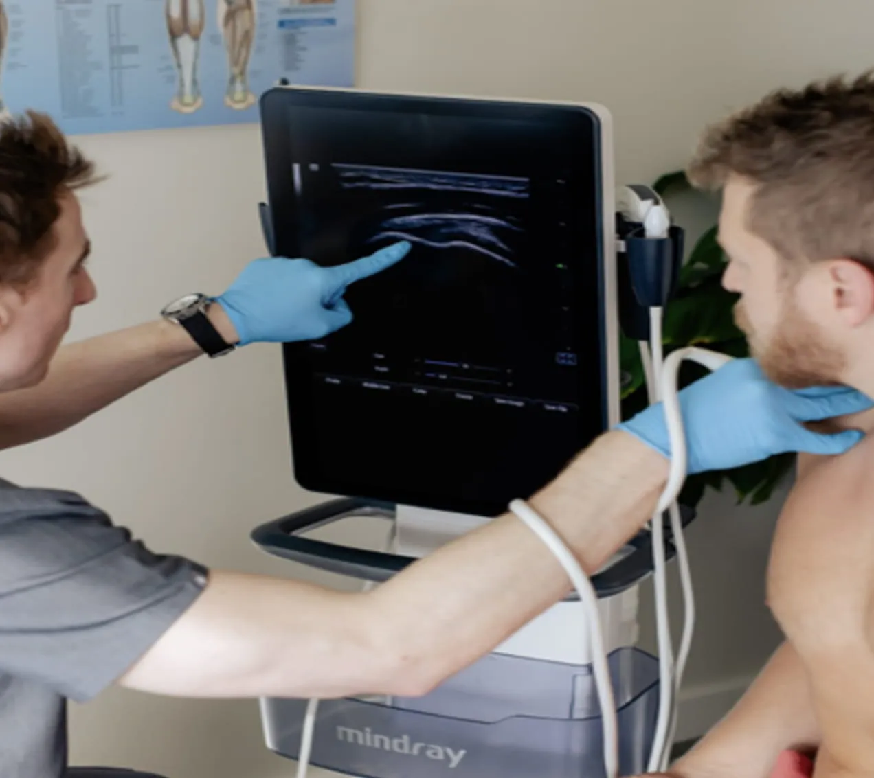 Medical professional wearing blue gloves using an ultrasound machine to scan a patient's neck while pointing at the ultrasound image on the screen.