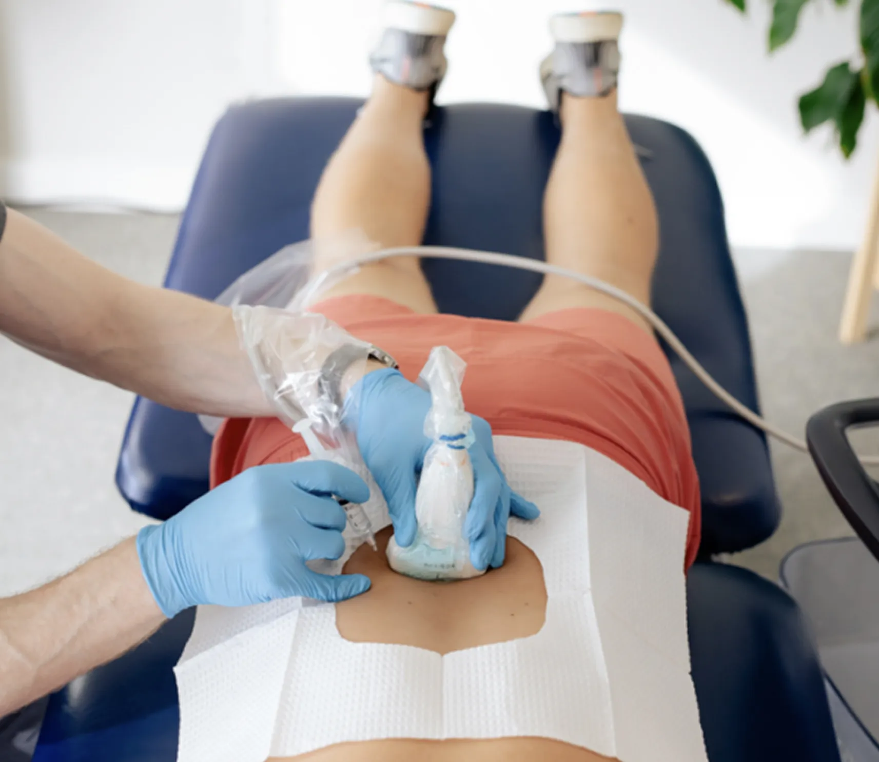Medical professional wearing blue gloves performing an ultrasound injection procedure on a patient's lower back.