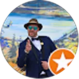 Man in a suit and bow tie wearing a hat and sunglasses posing outdoors with a mountainous landscape background.