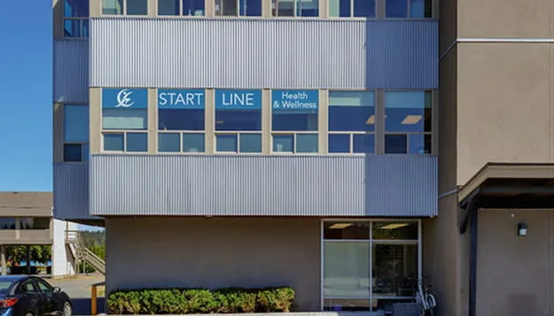 Exterior of a building with a window sign reading 'START LINE Health & Wellness' against a blue sky.
