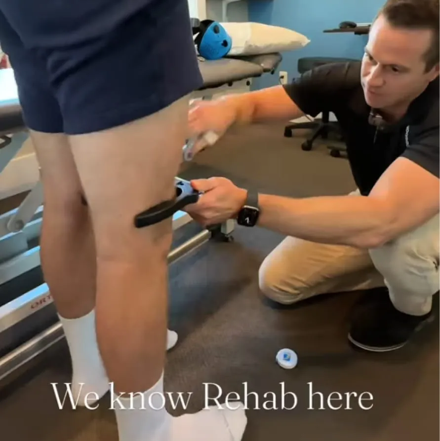 Therapist using a handheld device on a patient's thigh in a rehabilitation clinic.