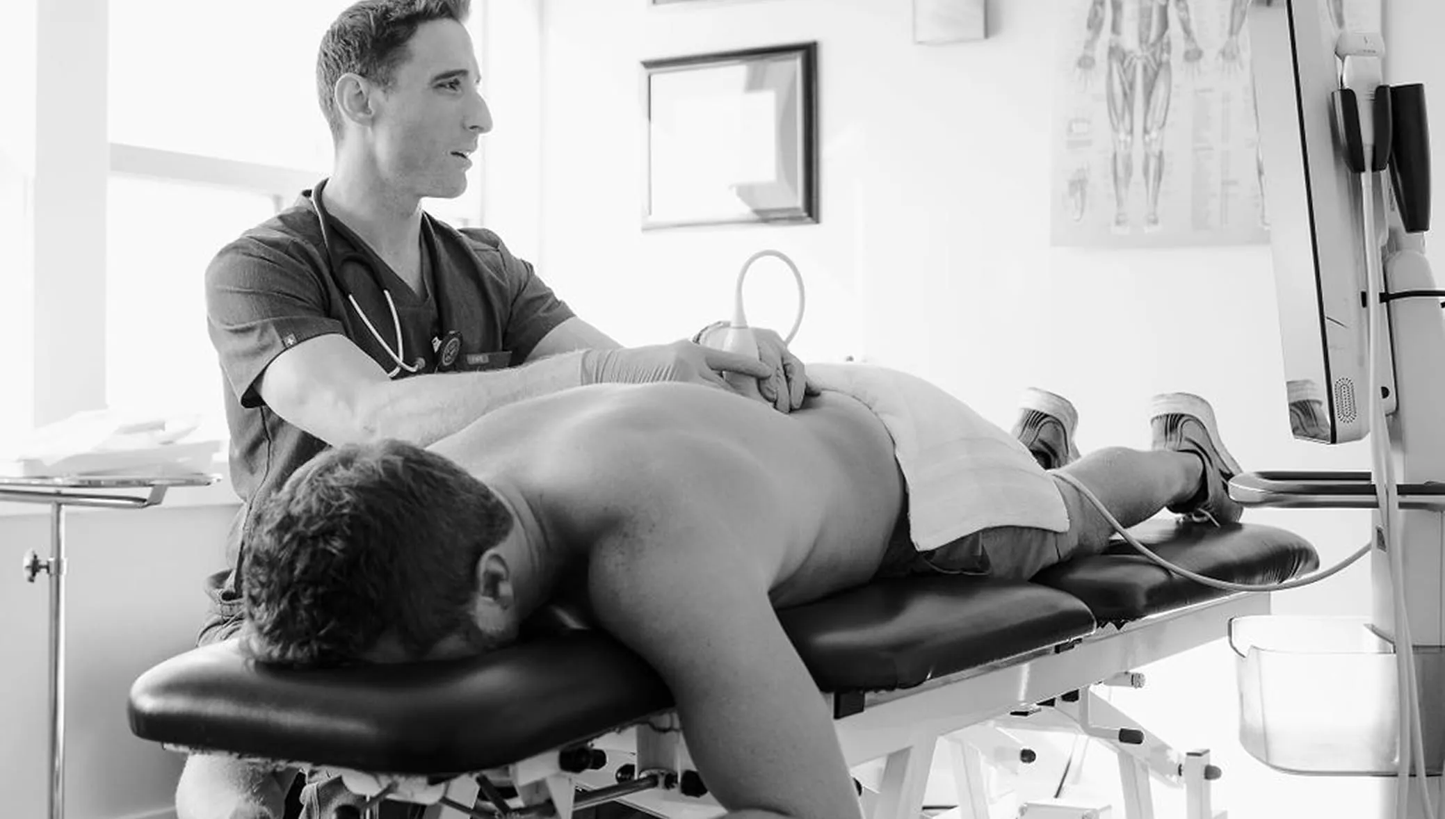 Medical professional performing an ultrasound scan on a man's lower back in a clinical setting.