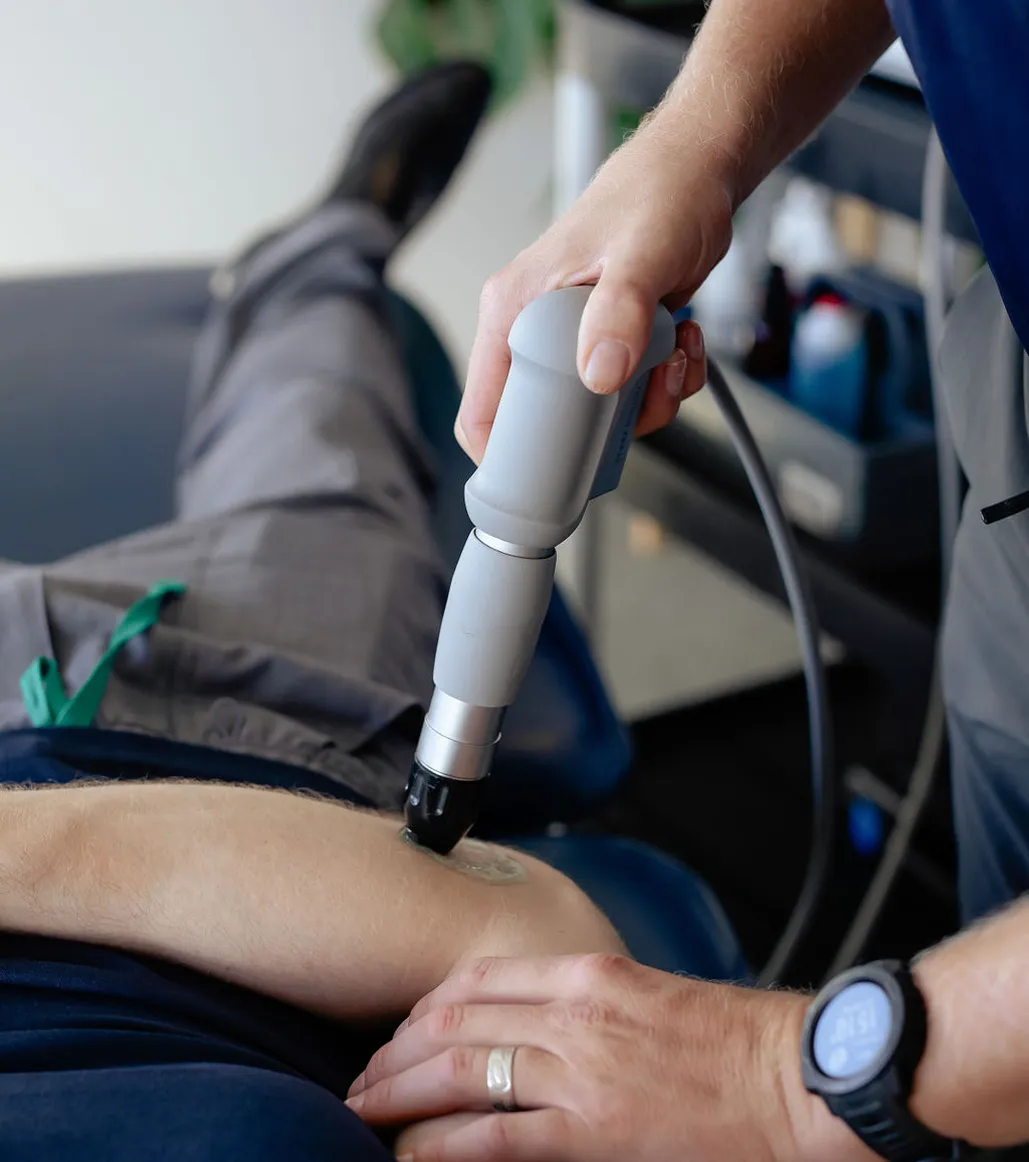 Therapist performing shockwave therapy on a patient's elbow using a handheld device.