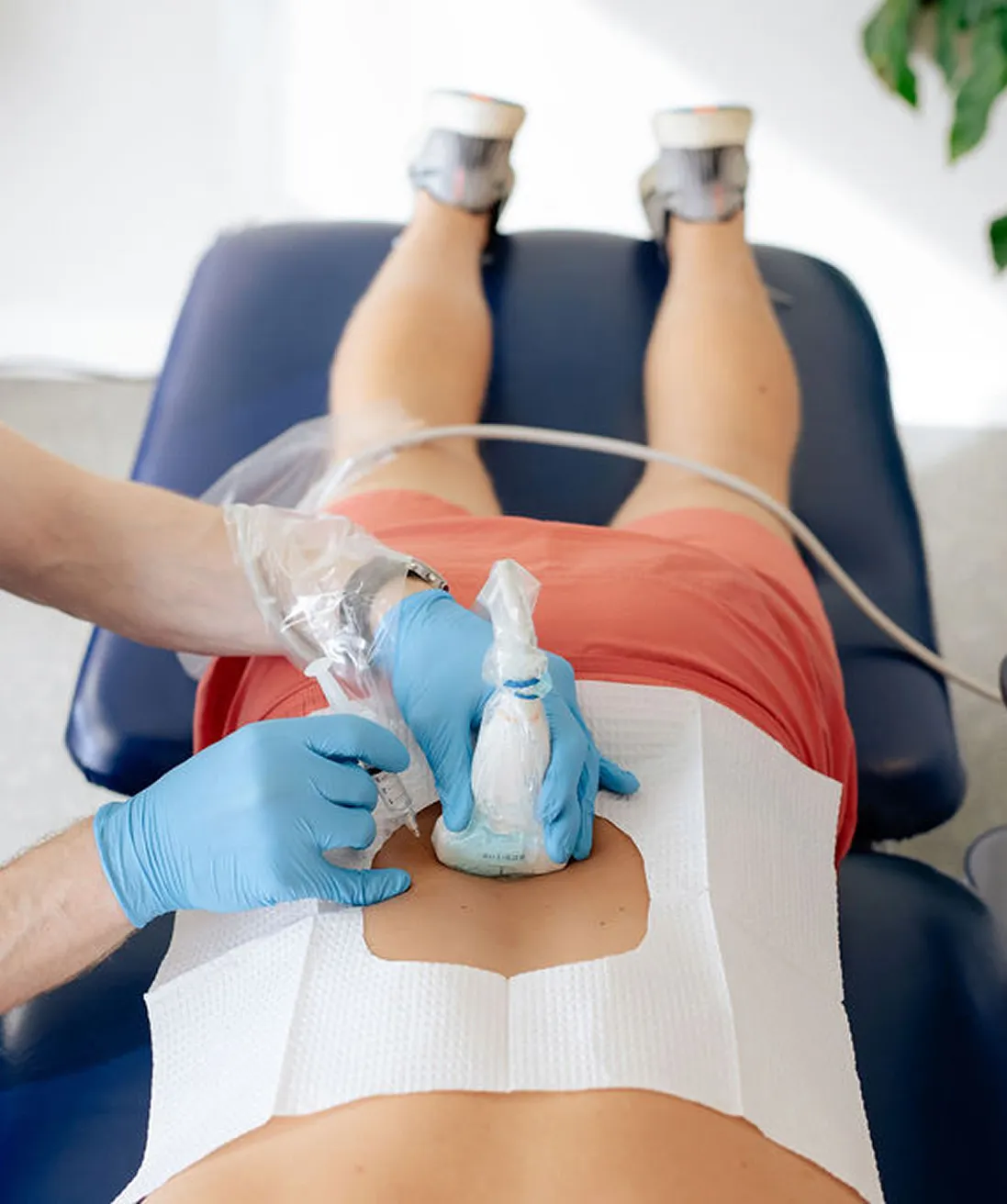 Medical professional wearing blue gloves performing ultrasound therapy on a patient's lower back.