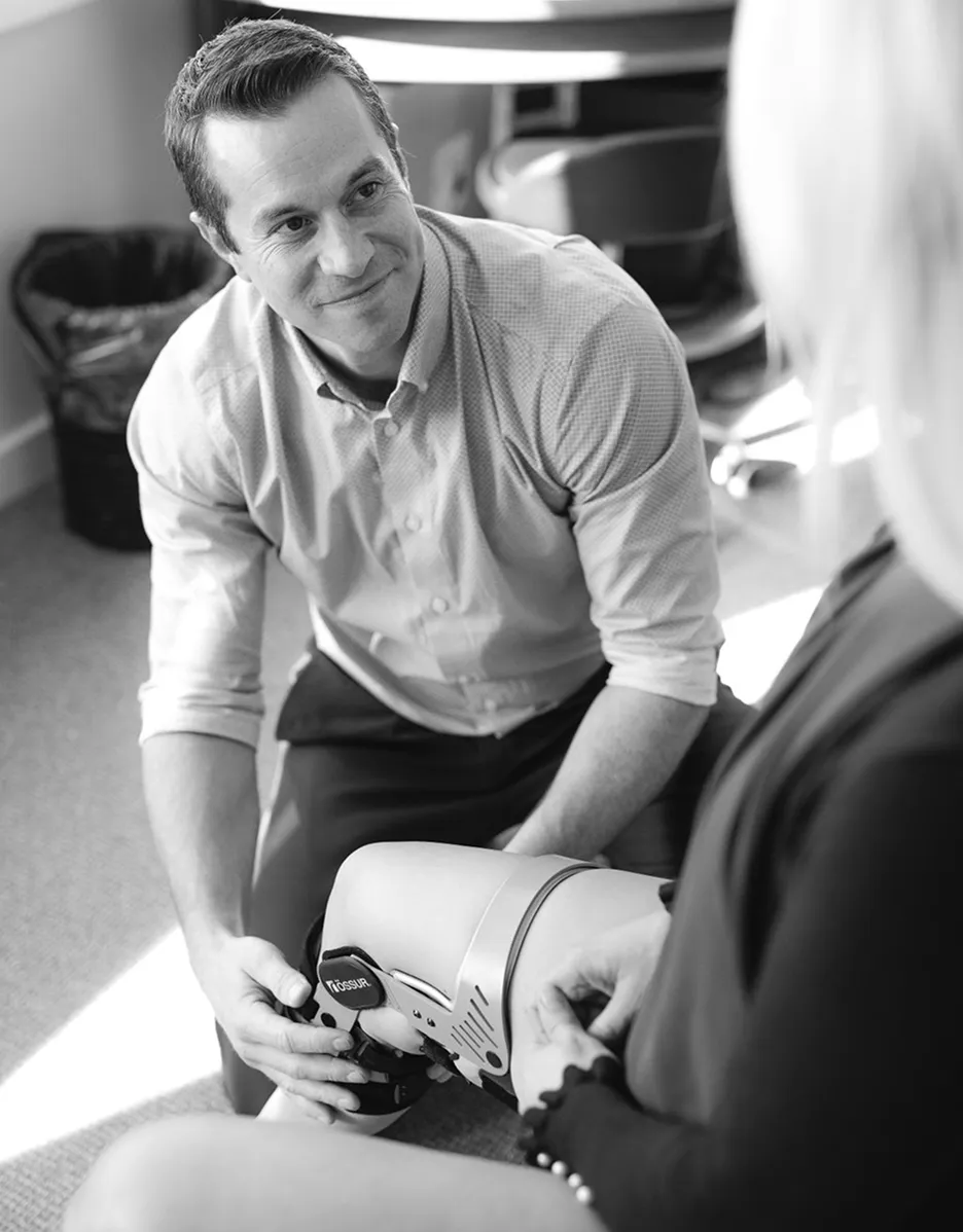 Man adjusting a prosthetic leg on a seated woman in a clinical setting.
