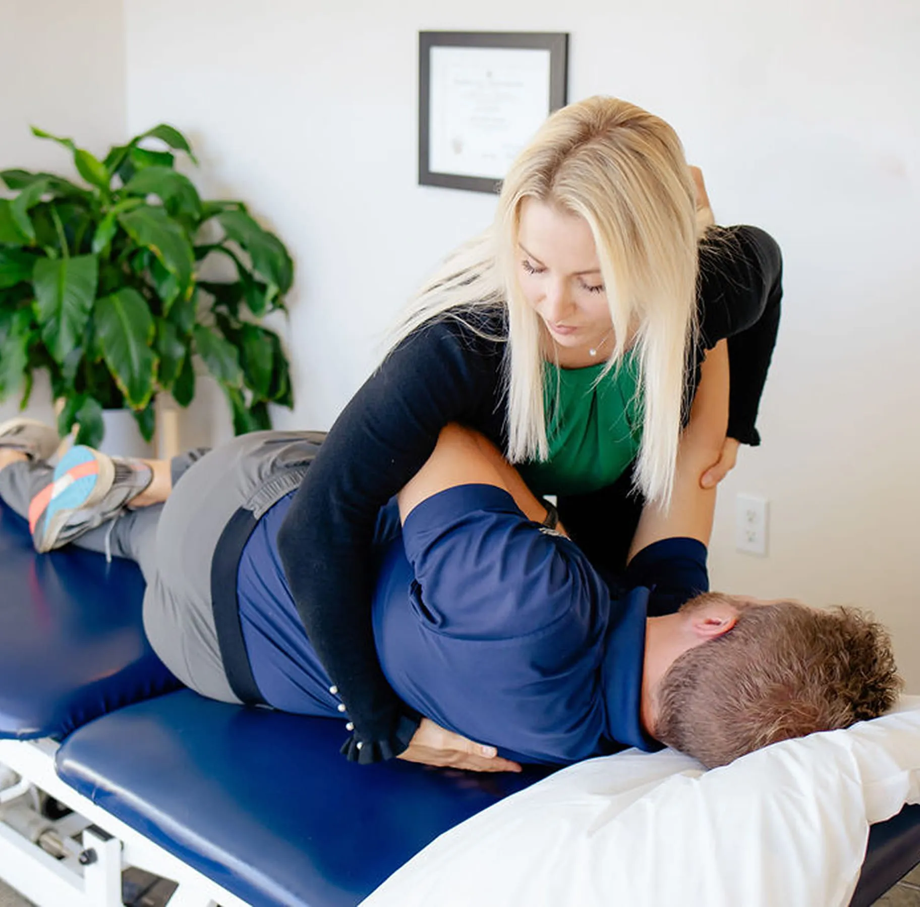 Physical therapist performing a spinal adjustment on a male patient lying on a treatment table.