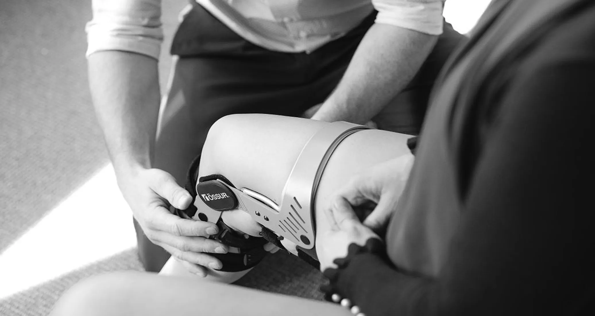Person fitting a knee brace on another person's leg, focusing on the knee support device.