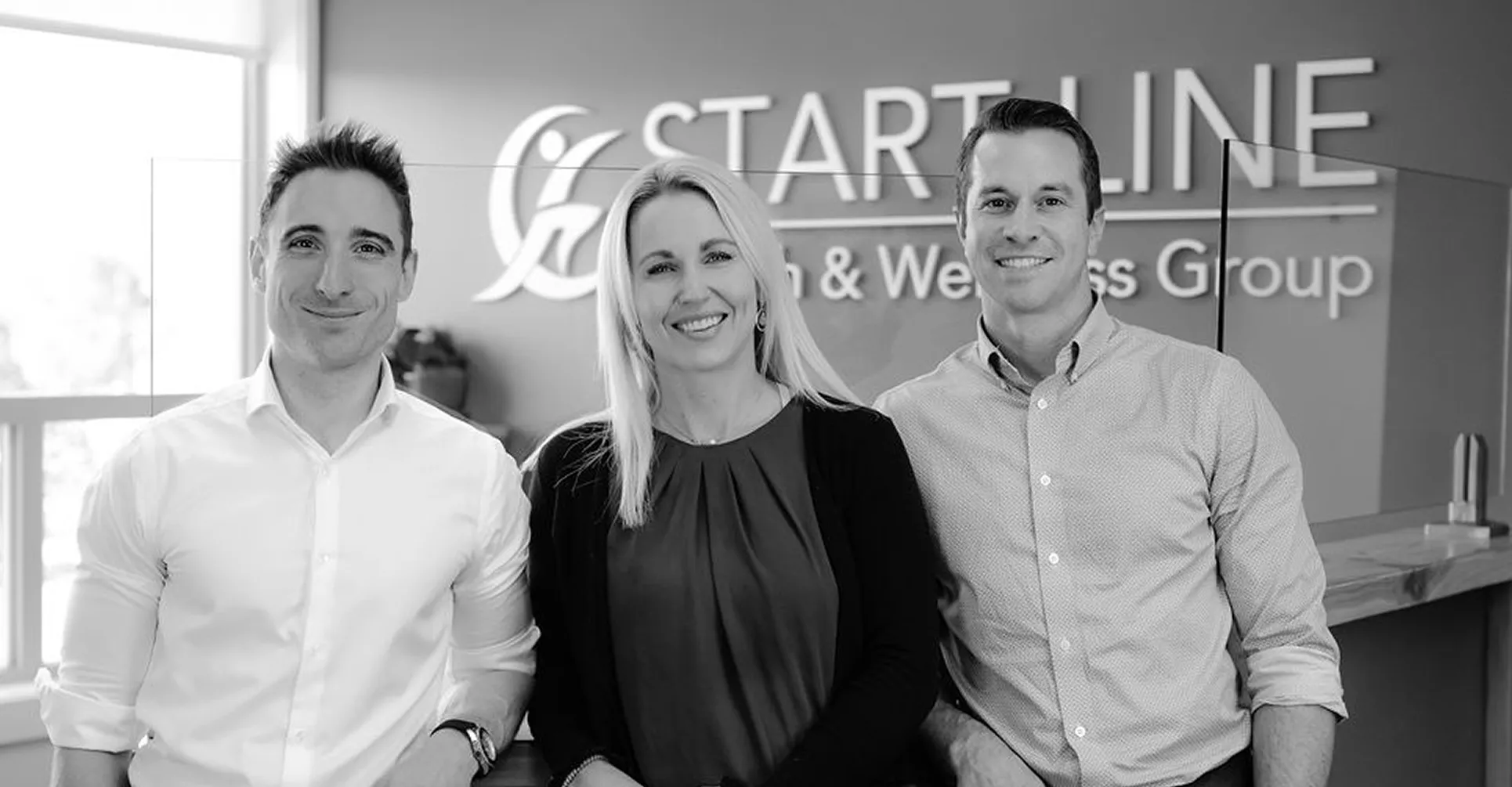 Three smiling professionals standing in front of a Start Line Health & Wellness Group sign.
