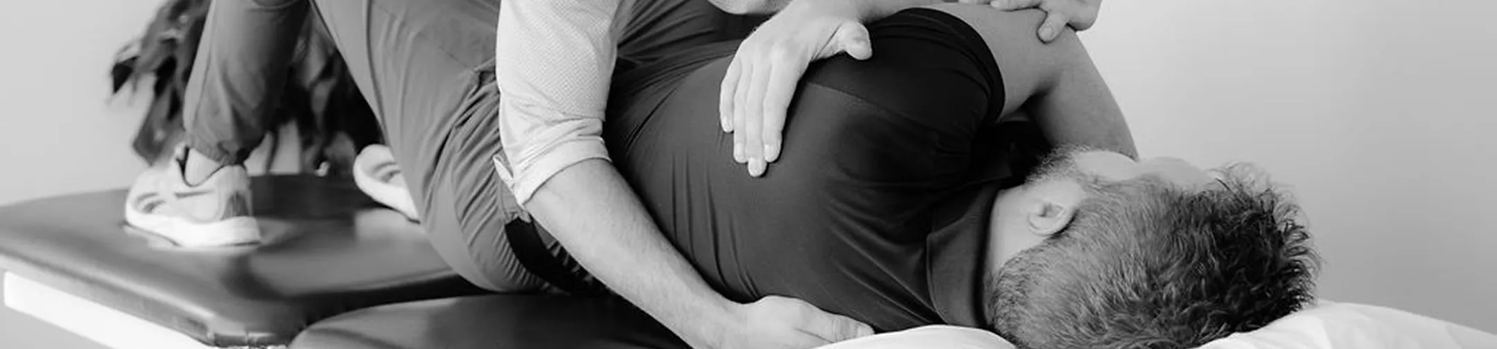 Physical therapist assisting a man lying on his side on a treatment table.