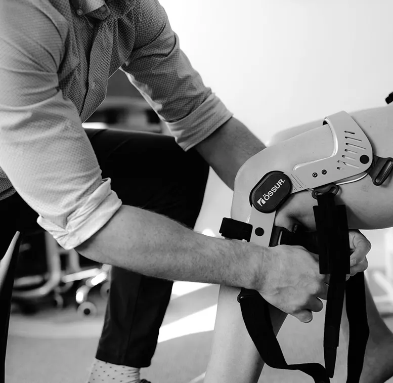 Person adjusting a knee brace labeled Össur on another person's leg.