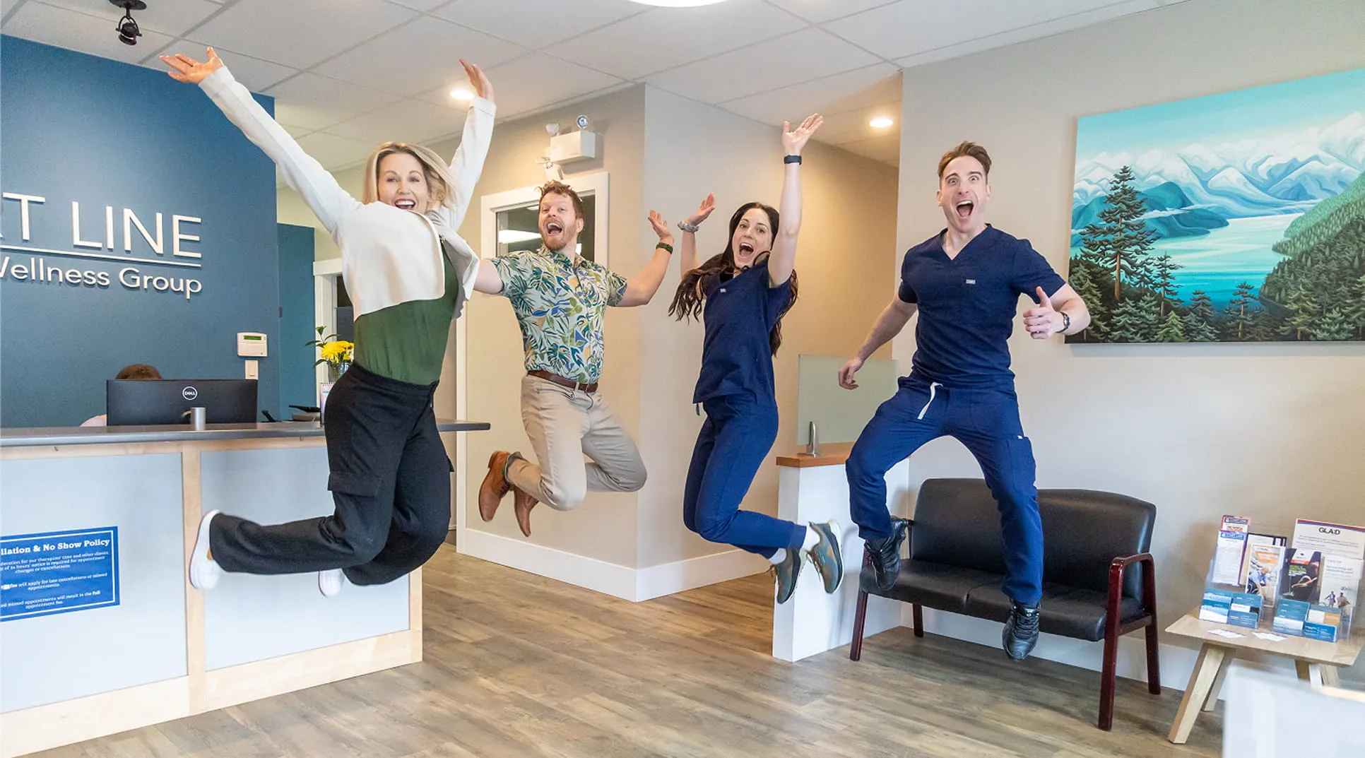 Four cheerful healthcare workers jumping with joy inside a clinic reception area.