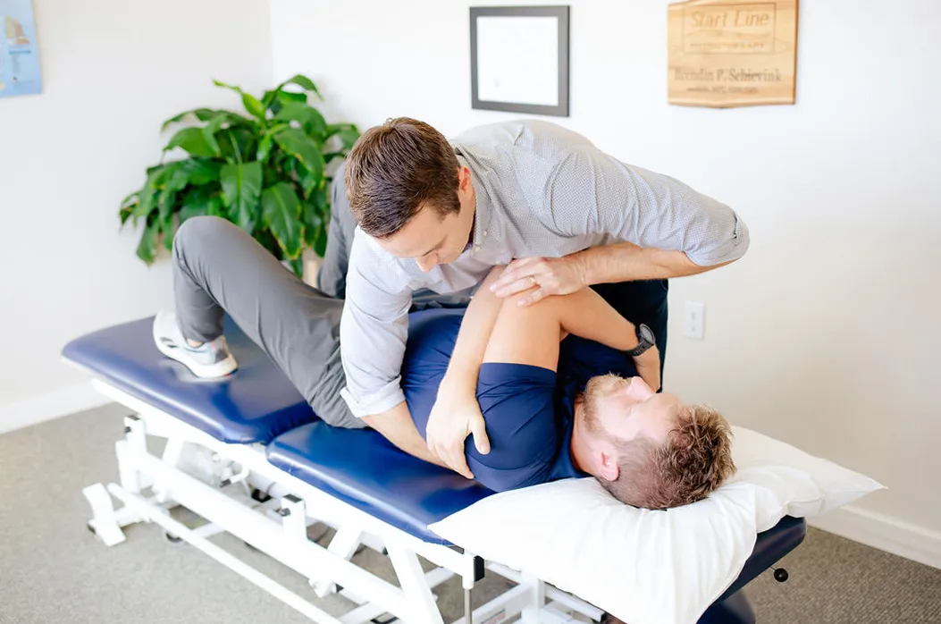 Physical therapist performing shoulder adjustment on a male patient lying on a treatment table.