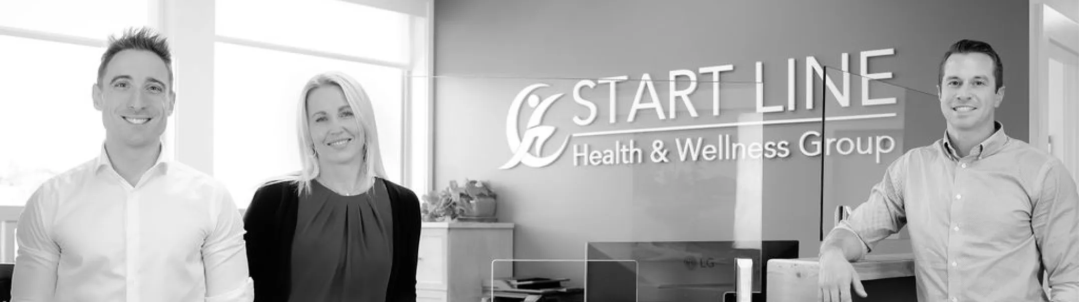 Three smiling professionals in an office with a Start Line Health & Wellness Group sign in the background.
