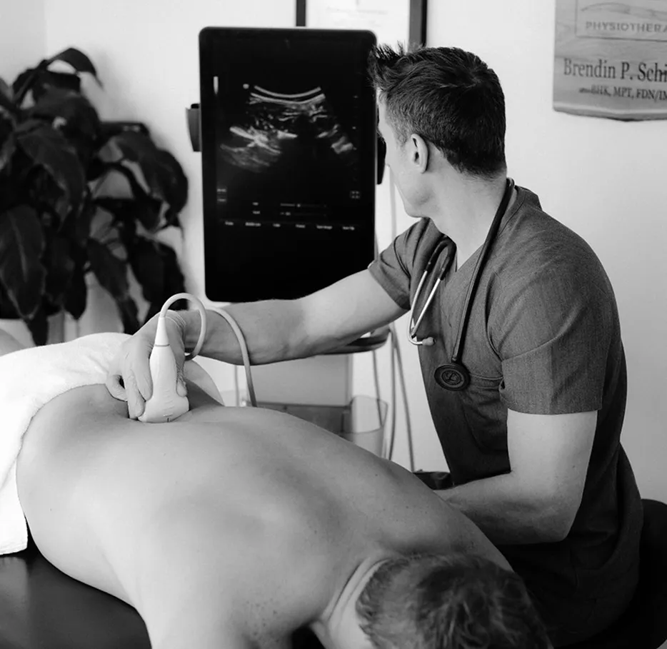 Medical professional using an ultrasound device on a patient's back with the ultrasound image displayed on a monitor.