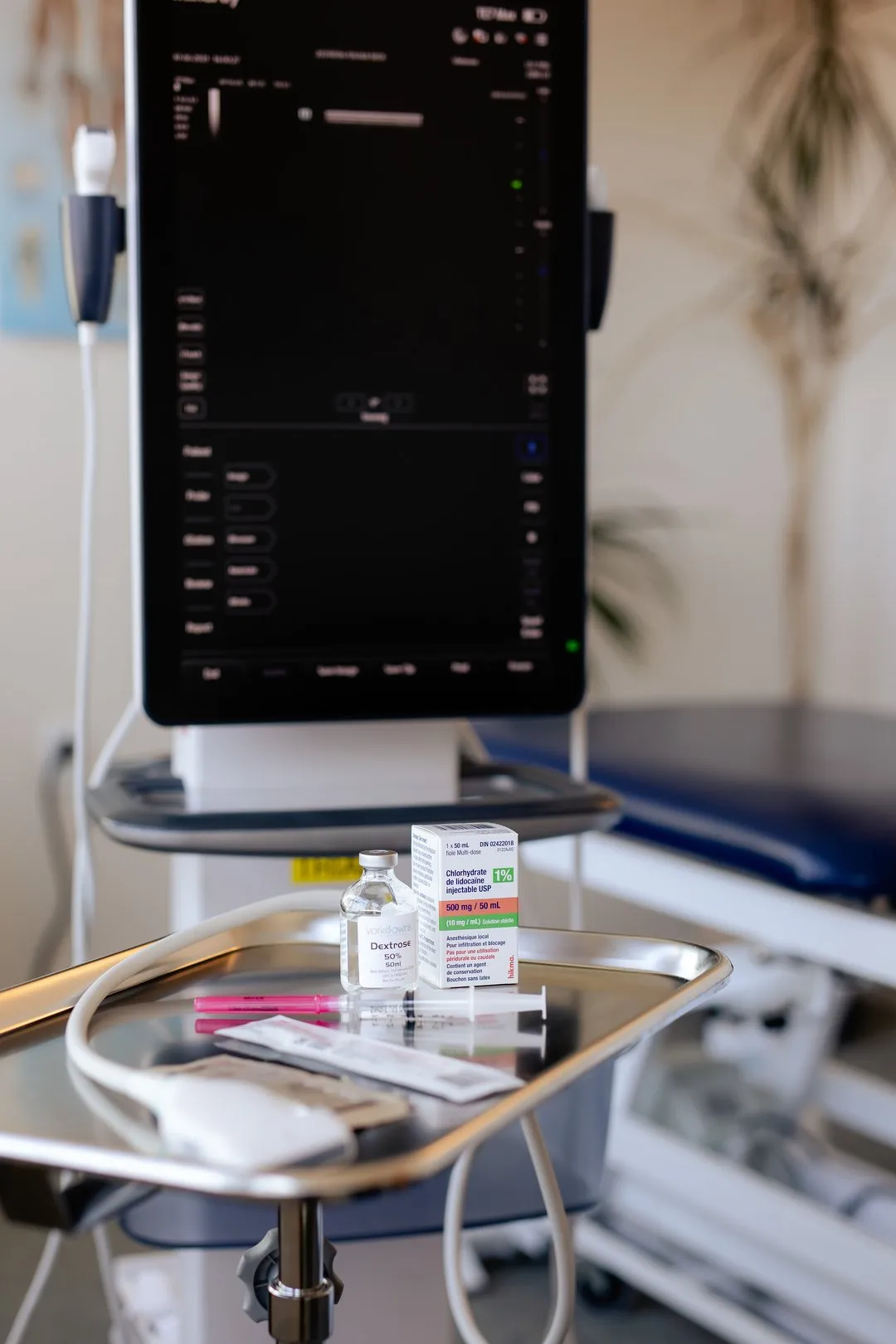 Medical tray with a vial of dextrose, lidocaine box, syringe, and tubing in a clinical exam room.