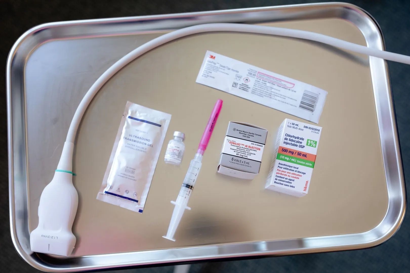 Medical tray with ultrasound probe, transmission gel, syringe, vial, and boxes of injectable medications.